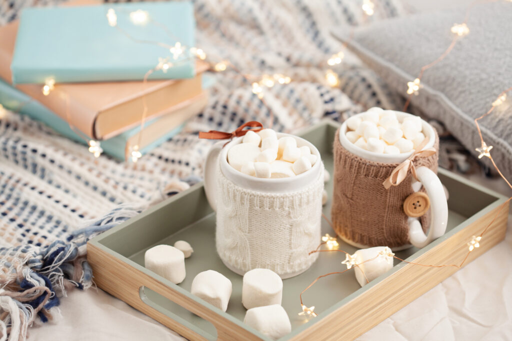 Winterlicher Lesespaß – Wintergeschichten für Kinder zum Lesen und Entdecken: Abgebildet sind Bücher und eine Tasse Kakao mit Marshmallows sowie eine Lichterkette.