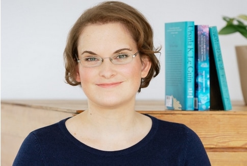 Buchsätze - Interview mit Kathrin Tordasi: Dargestellt ist die Autorin vor einer Kommode, auf der Bücher stehen.