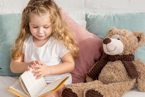 Rund ums Lesen - Spielerische Beschäftigung mit Büchern: Abgebildet ist ein Kind mit Buch und Teddy auf einem Bett.