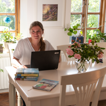 Steffi Bieber-Geske mit Laptop und Büchern am Esstisch sitzend